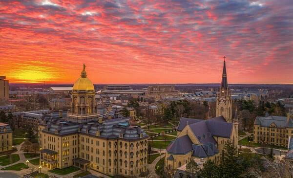 sun rises over the golden dome of the administration building and Sacred Heart Basilica at the University of Notre Dame.
