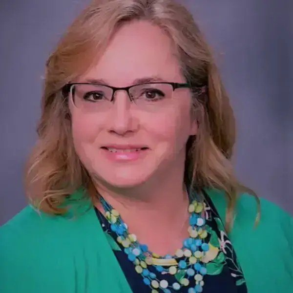 Blonde woman with glasses and a soft smile, wearing a bright green cardigan and a blue, green, and white beaded necklace.